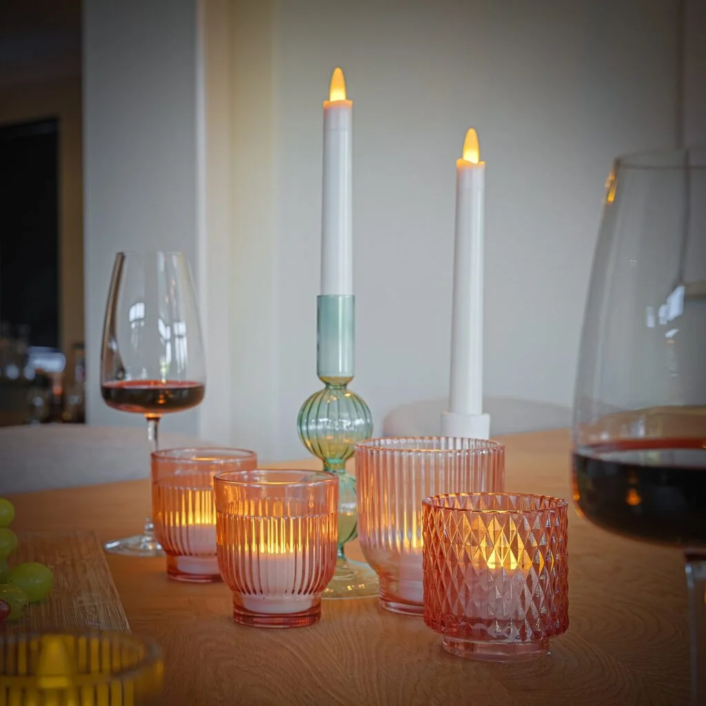 Een houten gedekte tafel met roze geribbelde glazen kaarshouders, een glas rode wijn, een deel van een kan en groene druiven, aangevuld met 6 oplaadbare dinerkaarsen (130u brandtijd, 270mm, warm wit) met afstandsbediening voor een gezellige sfeer.