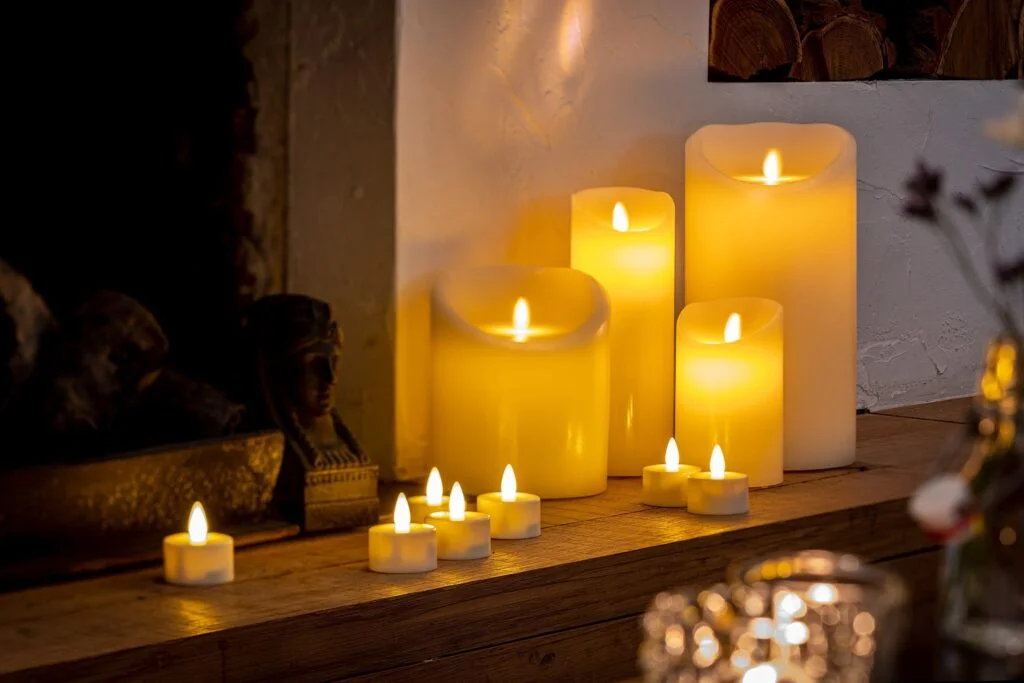 Een groep oplaadbare LED-kaarsen (7,5 cm x 20 cm, 30 uur brandtijd, met afstandsbediening) gloeit warm op een houten schoorsteenmantel en zorgt samen met een paar kleine waxinelichtjes voor een gezellige sfeer.